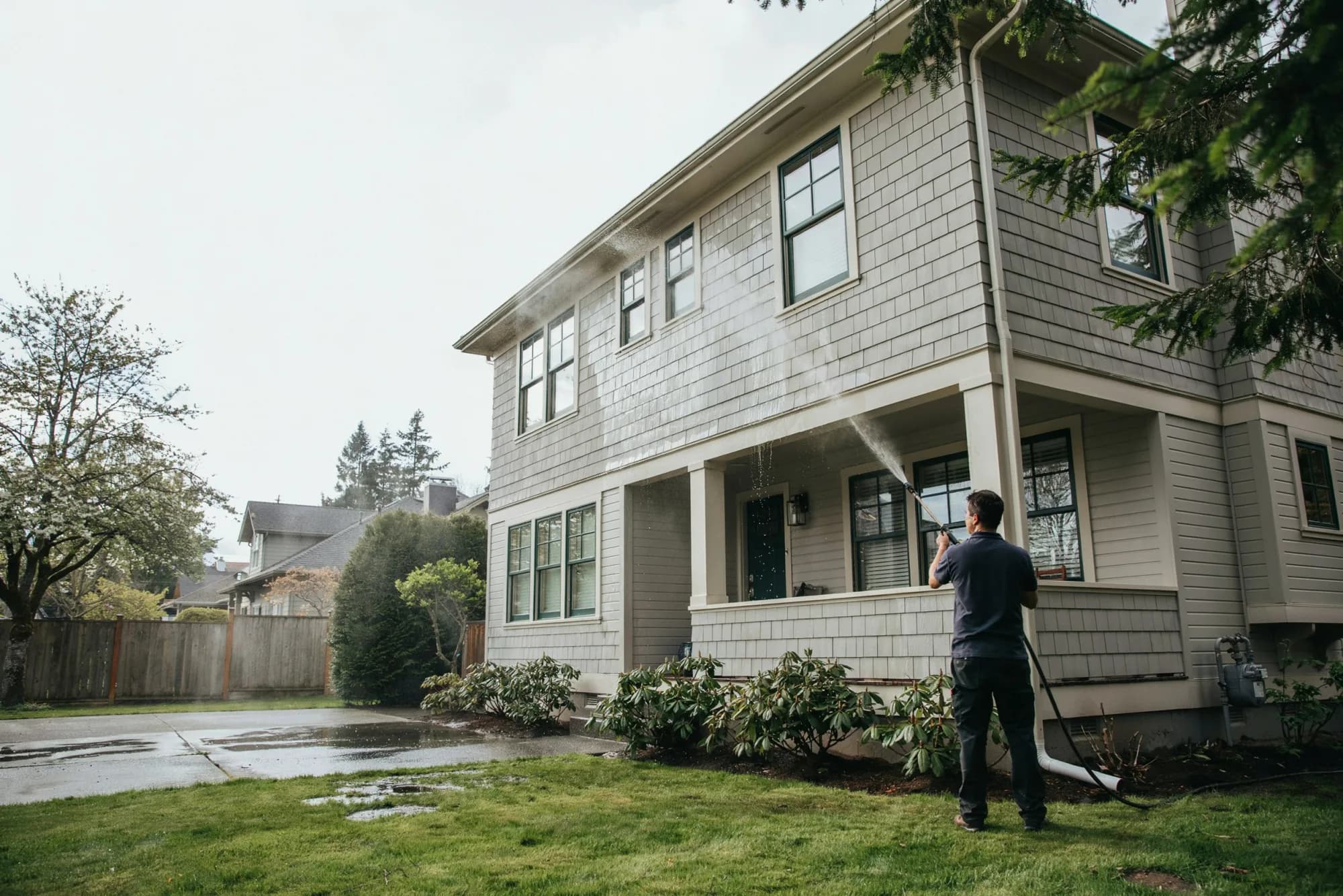 A technician soft-washing the siding of a two-story Portland home from the lawn