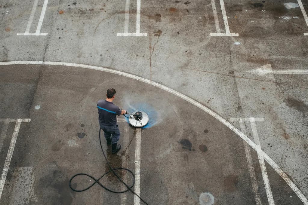 Overhead view of a technician running a surface cleaner across a parking lot, cutting a clean arc