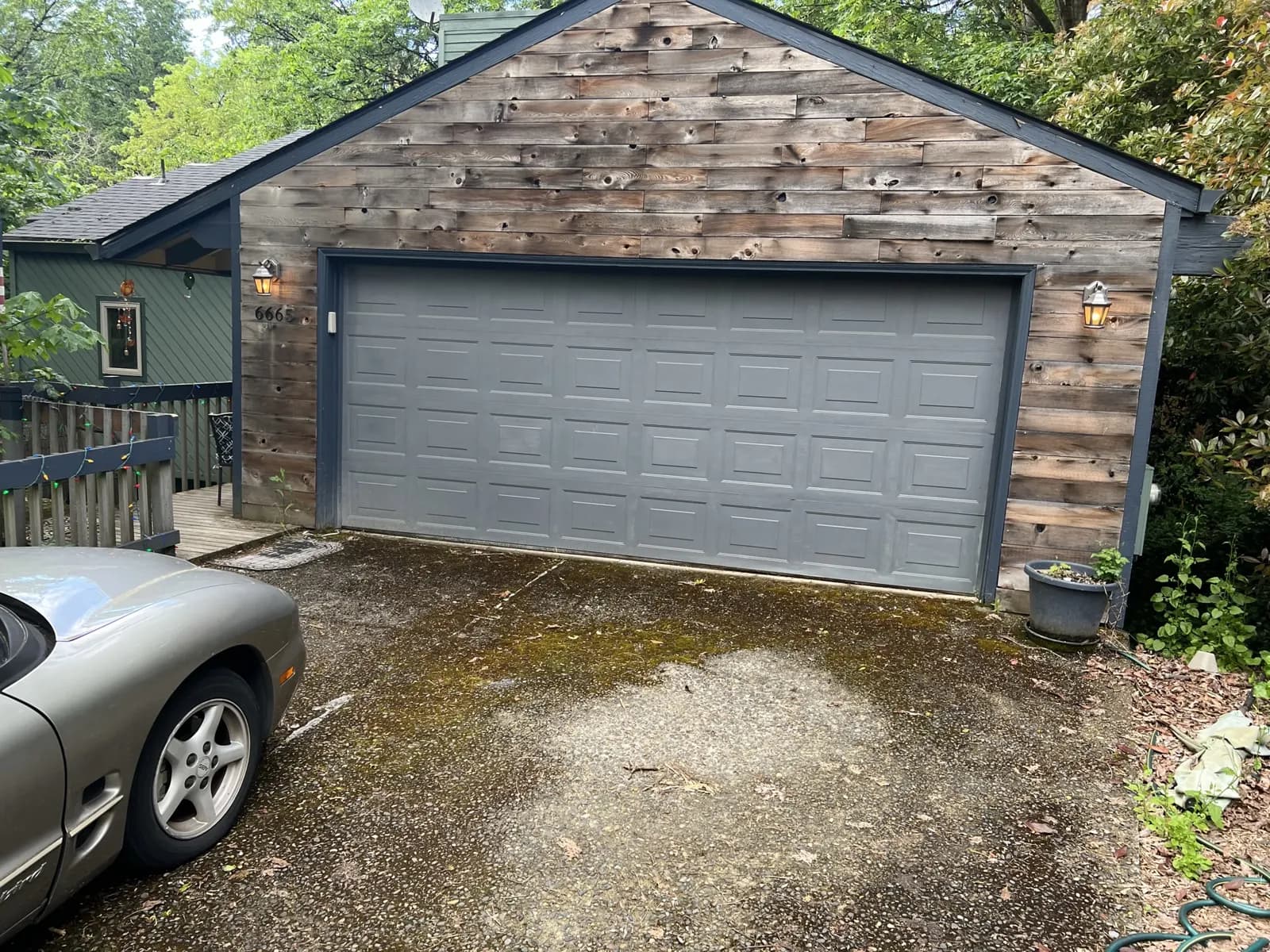 Residential driveway covered in moss and grit in front of a cedar garage