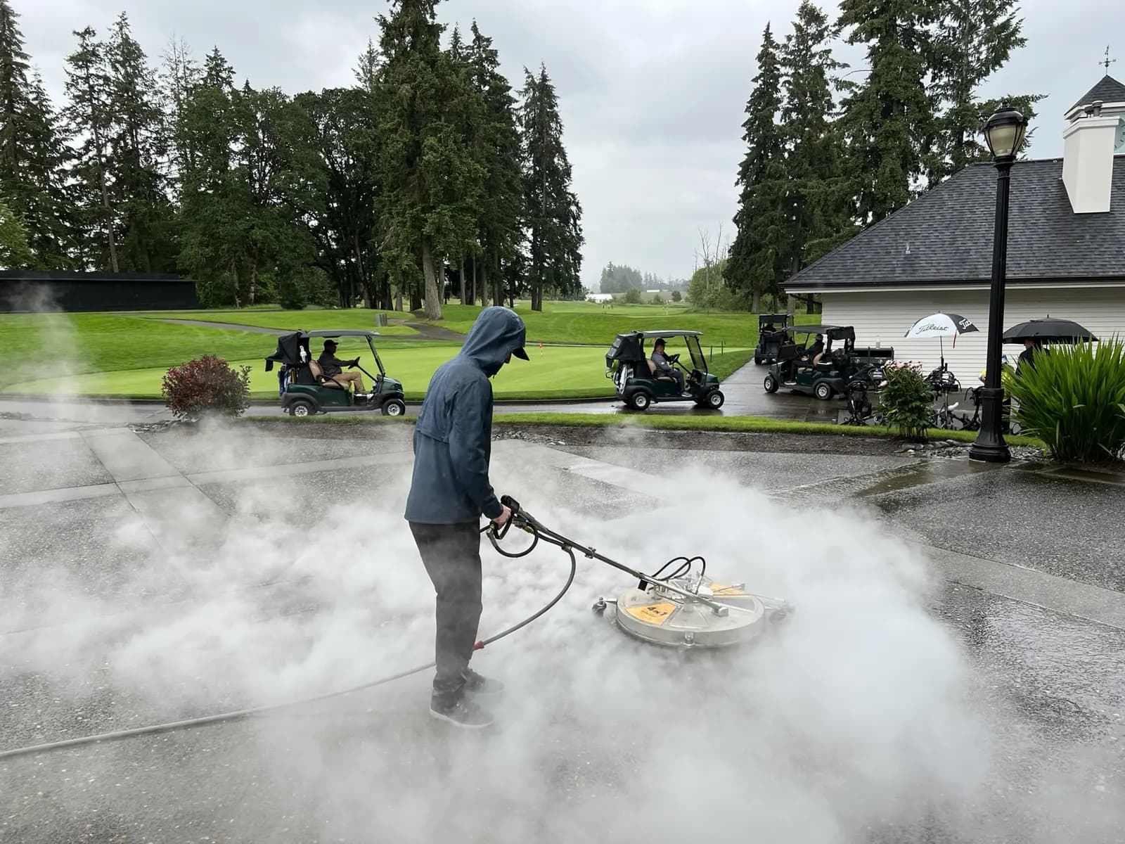 Technician guiding a surface cleaner through a cloud of steam on a clubhouse walkway