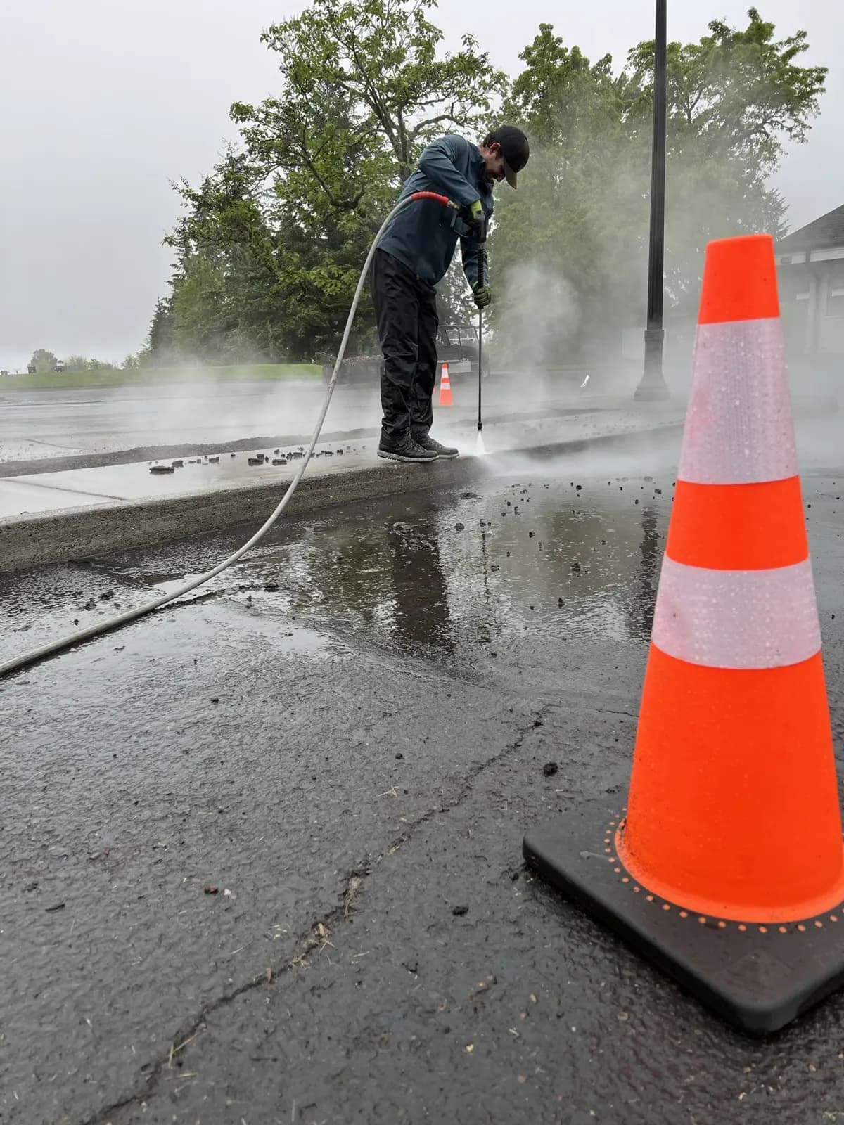 Technician washing a curb edge behind an orange traffic cone